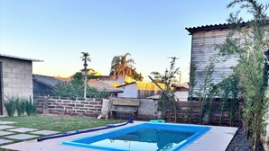 A rectangular swimming pool with a blue interior, surrounded by a concrete deck and a grassy lawn. - Kiosk with Private Pool (Sapucaia do Sul)