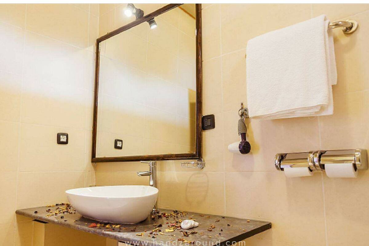 Un baño con lavamanos blanco, un espejo, toallero y soporte para papel higiénico.