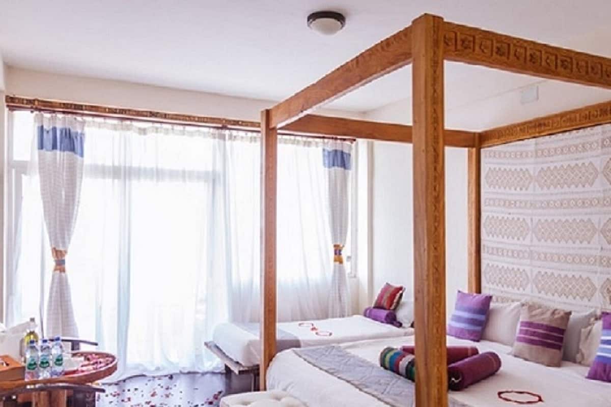 Una cama con dosel sobre un armazón de madera, dos mesitas de noche y un papel tapiz estampado.