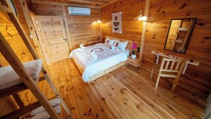 Un dormitorio de cabaña de madera con una cama, una silla de madera, una mesita de noche y un espejo en la pared.