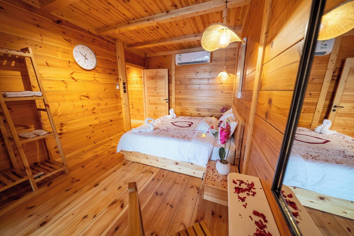 A wooden cabin bedroom with a bed, a ladder, a wall clock, and an air conditioning unit.