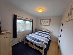 A bedroom with a bed, a dresser, a window with curtains, a painting on the wall, and a ceiling light.