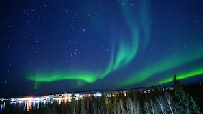 Cielo nocturno con auroras boreales sobre un pueblo, con edificios reflejándose en el agua.