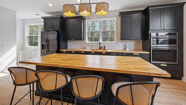 Una cocina moderna con armarios oscuros, una isla de madera y tres sillas de mimbre.