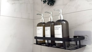 Une étagère de salle de bain avec trois bouteilles étiquetées « Shampoing », « Gel douche » et « Après-shampoing ».