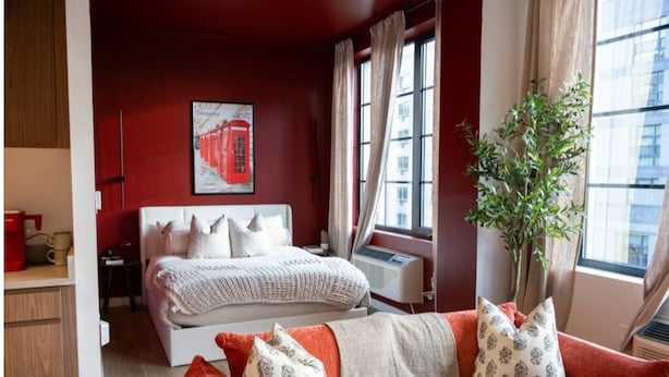 Une chambre à coucher avec un lit, une table de chevet, une fenêtre avec des rideaux, une plante et un canapé rouge et blanc.