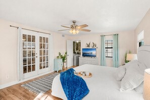 Ein Schlafzimmer mit einem Bett, einem Deckenventilator, einem Fernseher, einer Kommode und einer Tür mit Glasfeldern.