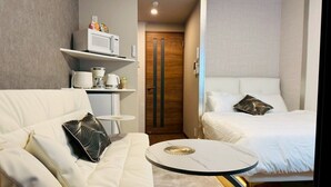 A modern hotel room with a white sofa, a round coffee table, a bed with white bedding, and a wooden door. - New! LuxurySweet Hakata Ekiminami 52 ・Max 3~4 people, 5 min. drive from Hakata Station, New construction (Fukuoka Hakata Ward)