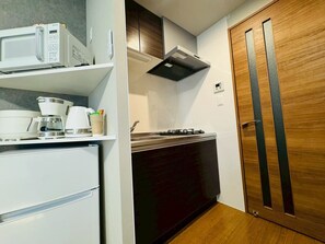 Una kitchenette compacta con microondas, cafetera y cocina a gas.