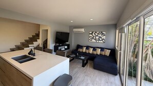 A modern living room with a sofa, TV, and a kitchen area with a sink and counter. - Luxury Townhouse 6 Minutes from Beach & Casino (Oranjestad)