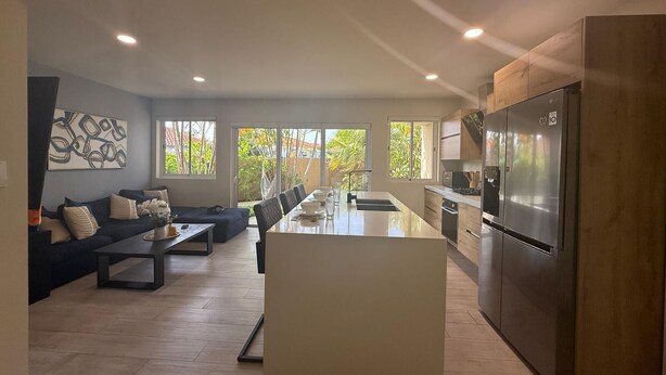 A modern kitchen with a central island, a dining area with a long table, and a living room with a sofa and a coffee table. - Luxury Townhouse 6 Minutes from Beach & Casino (Oranjestad)