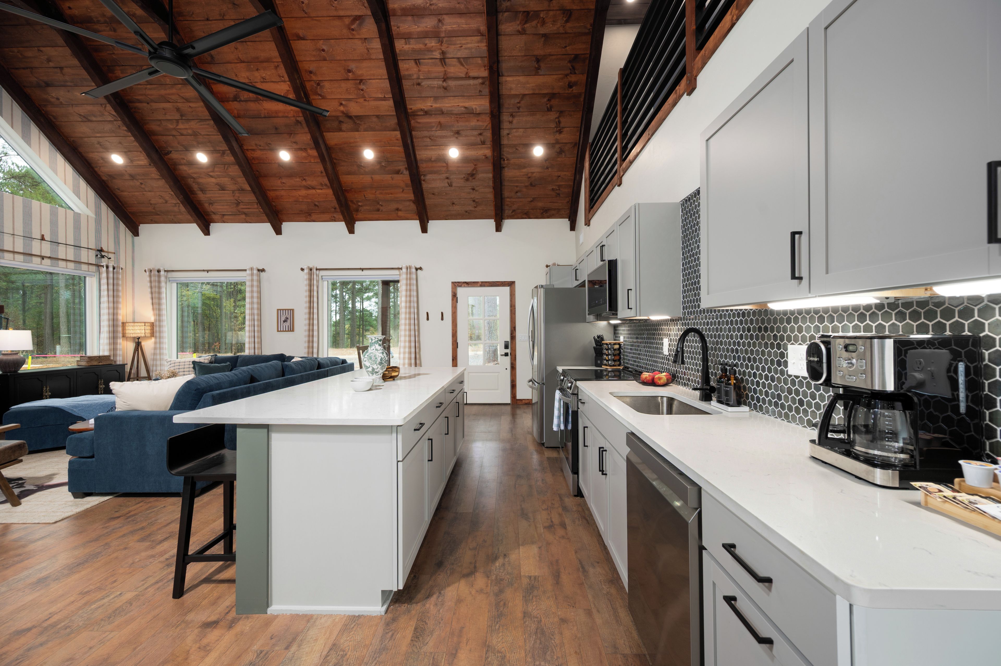 A modern kitchen with white cabinets, a central island, and a dining area with a blue sofa.