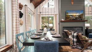 Un coin repas avec une longue table dressée pour six personnes, entourée de chaises bleues, d’une cheminée et d’une tête de cerf accrochée au mur.