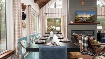A dining area with a long table set for six, surrounded by blue chairs, a fireplace, and a mounted deer head.