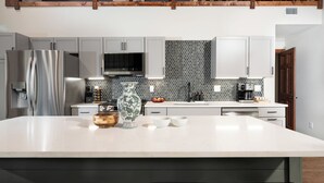 Une cuisine moderne dotée d’un grand îlot central, de meubles gris, d’un pare-feu hexagonal et d’une poutre en bois au plafond.