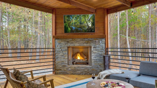L’intérieur chaleureux d’un chalet avec une cheminée en pierre, des meubles en bois et un grand téléviseur fixé au-dessus.