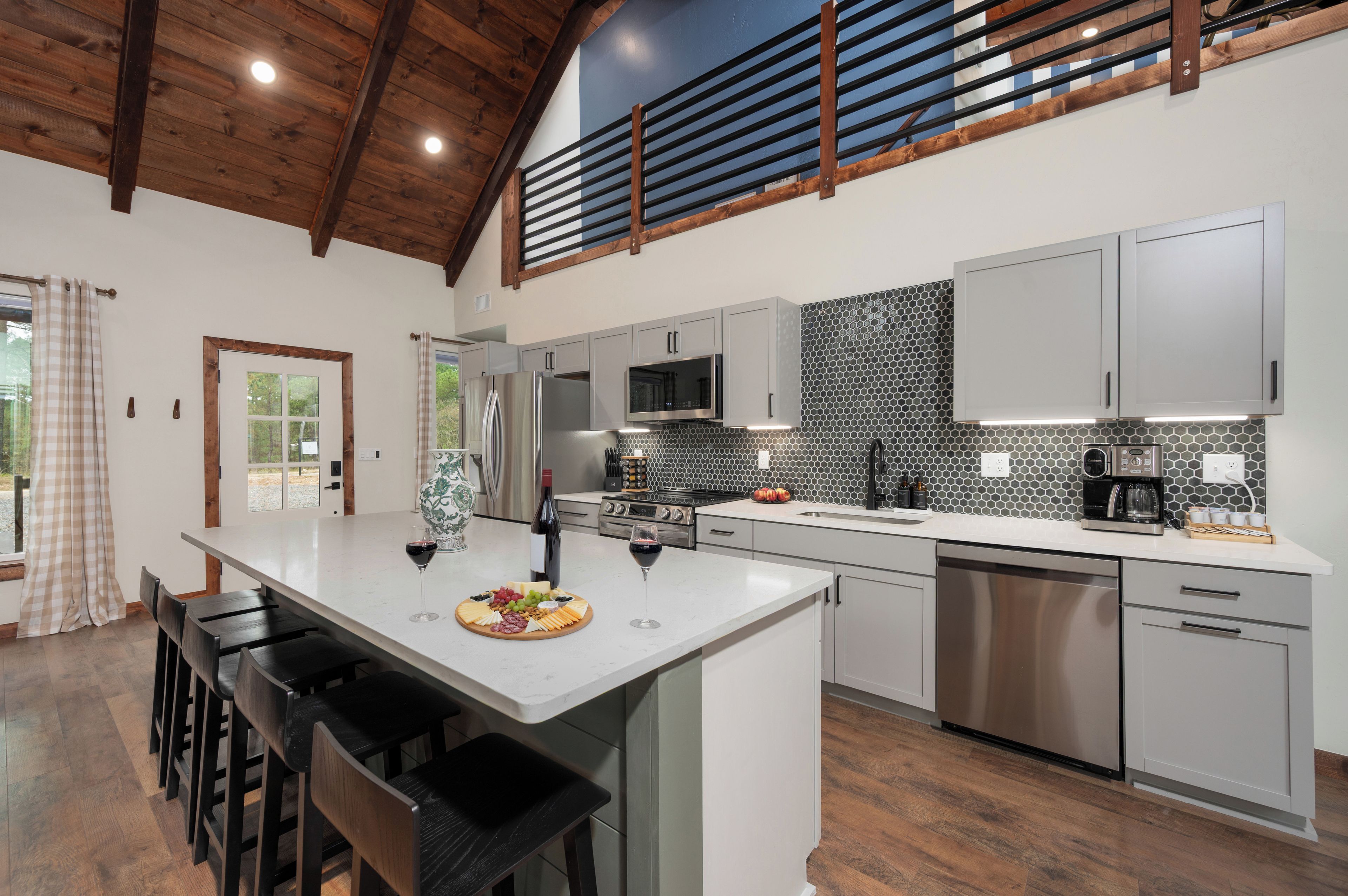A modern kitchen with a large island, stainless steel appliances, and a herringbone tile backsplash.