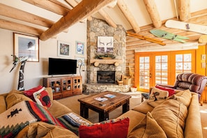 A cozy living room with a stone fireplace, wooden beams, a leather armchair, and a television. - Experience luxury at Deer Valley Pine Inn 4, a ski-in/ski-out townhome in Park City. (Park City)