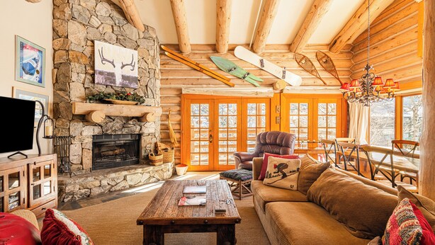 Ein Blockhaus-Interieur mit Kamin aus Stein, Holzmöbeln und Ski-Ausrüstung.