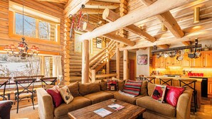 Ein Blockhaus-Interieur mit einer Holztreppe, einem Essbereich und einem Wohnzimmer mit Sofas und einem Couchtisch.