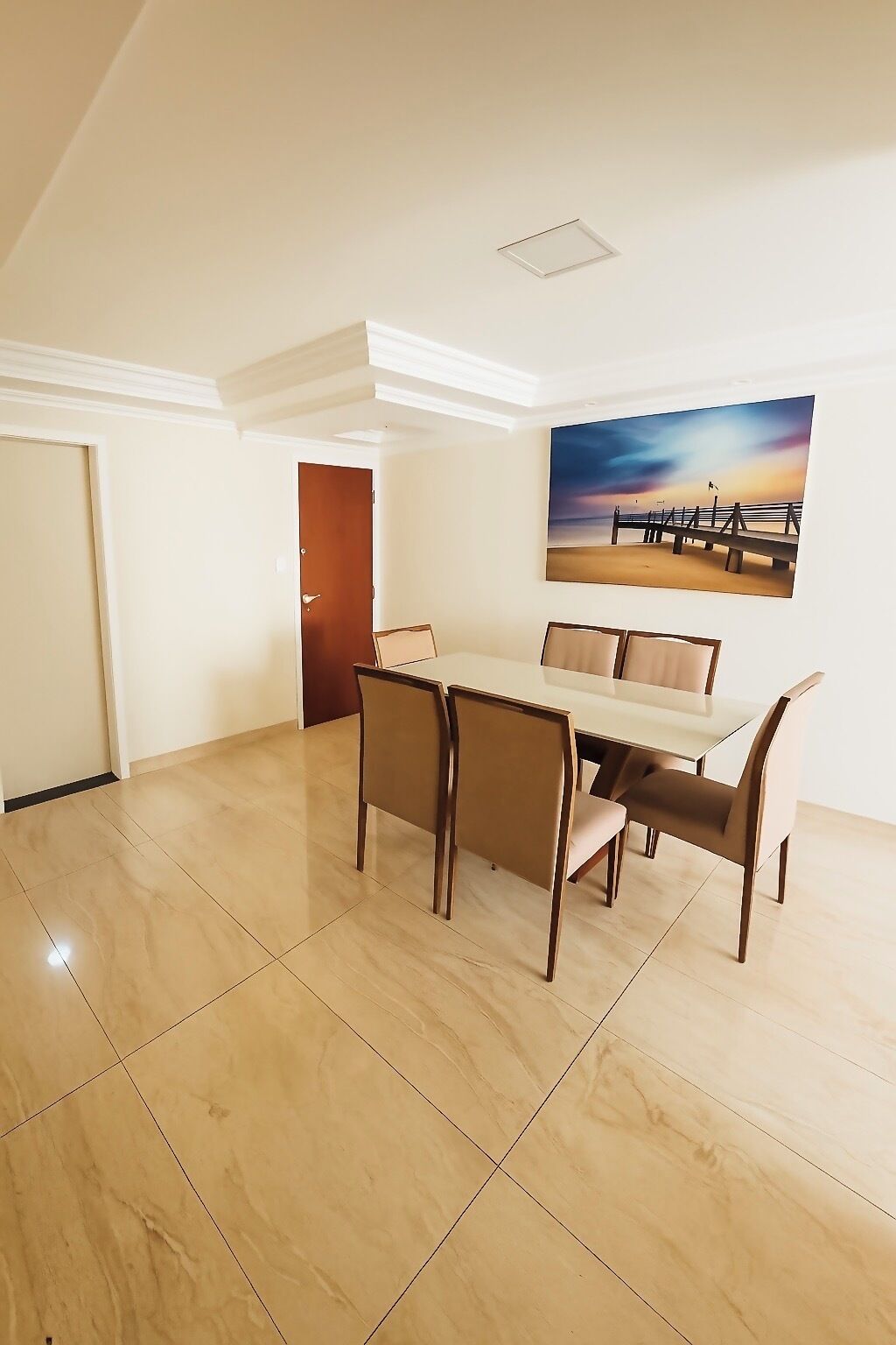 Un coin repas avec une table et des chaises, un tableau accroché au mur et une porte visible au fond.