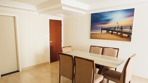 Uma área de refeições com mesa e cadeiras, um quadro na parede e uma porta ao fundo.