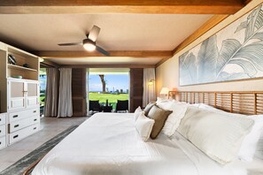 Ein Schlafzimmer mit einem großen Bett, einem Deckenventilator, Blick ins Freie und einem Essbereich mit Stühlen.