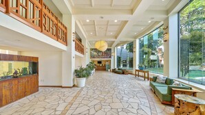 Un vestíbulo espacioso con suelo de piedra, mostrador de recepción de madera, un sofá verde y ventanas amplias con vistas al exterior.