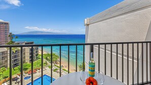 A balcony with a view of a beach and ocean, a bottle of Sun POF, and a table with two glasses. - Ocean view 2-bedroom Condo in Lahaina, West Maui - Kaanapali Shores 903 (Lahaina)