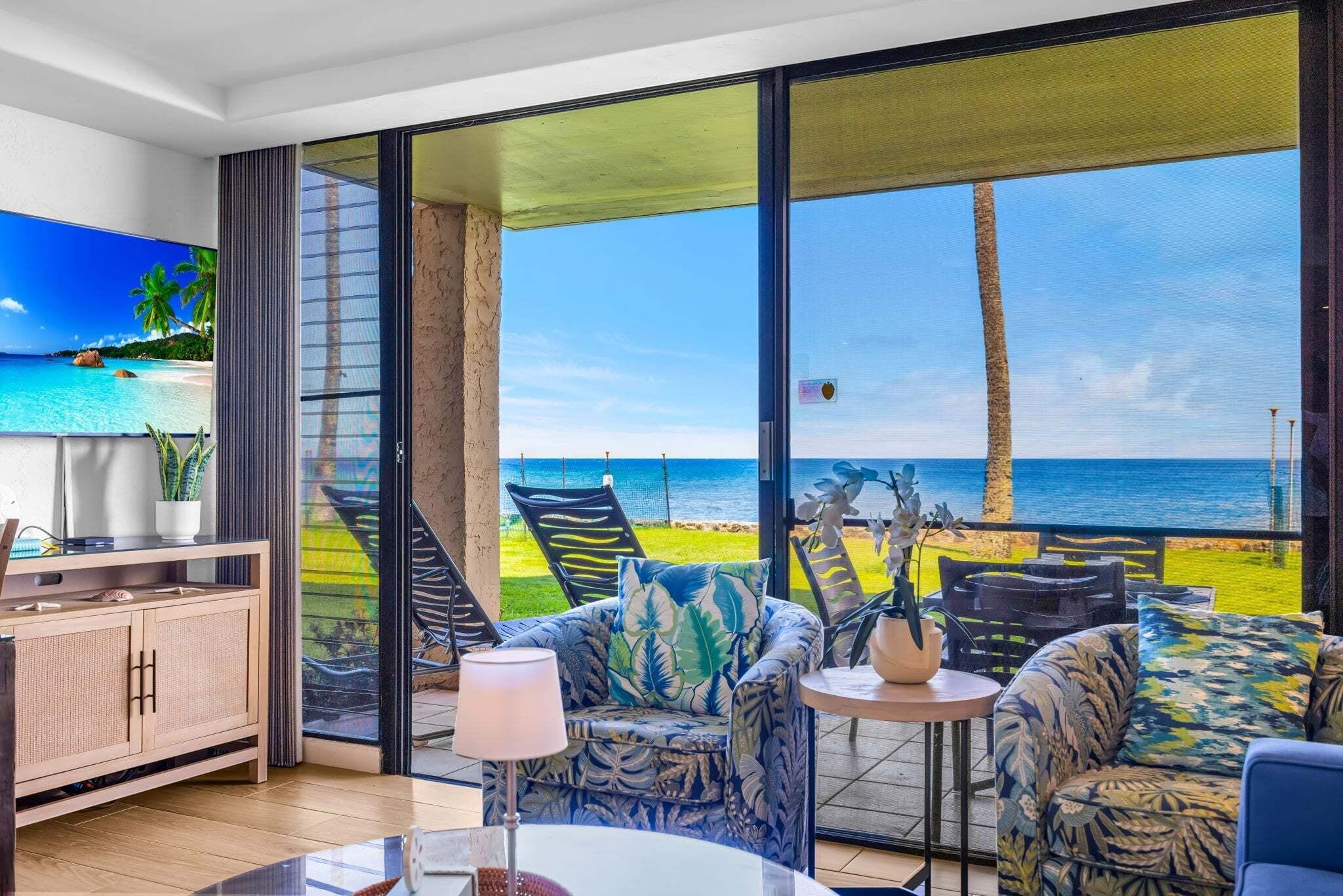 A room with a large sliding glass door leading to a beach view, a sofa, a small table, and a cabinet.