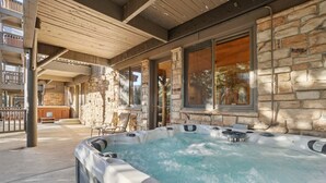 Ett område med ett bubbelbad, omgivet av stenmurar och stora fönster, en täckt uteplats och utsikt över det omgivande landskapet.