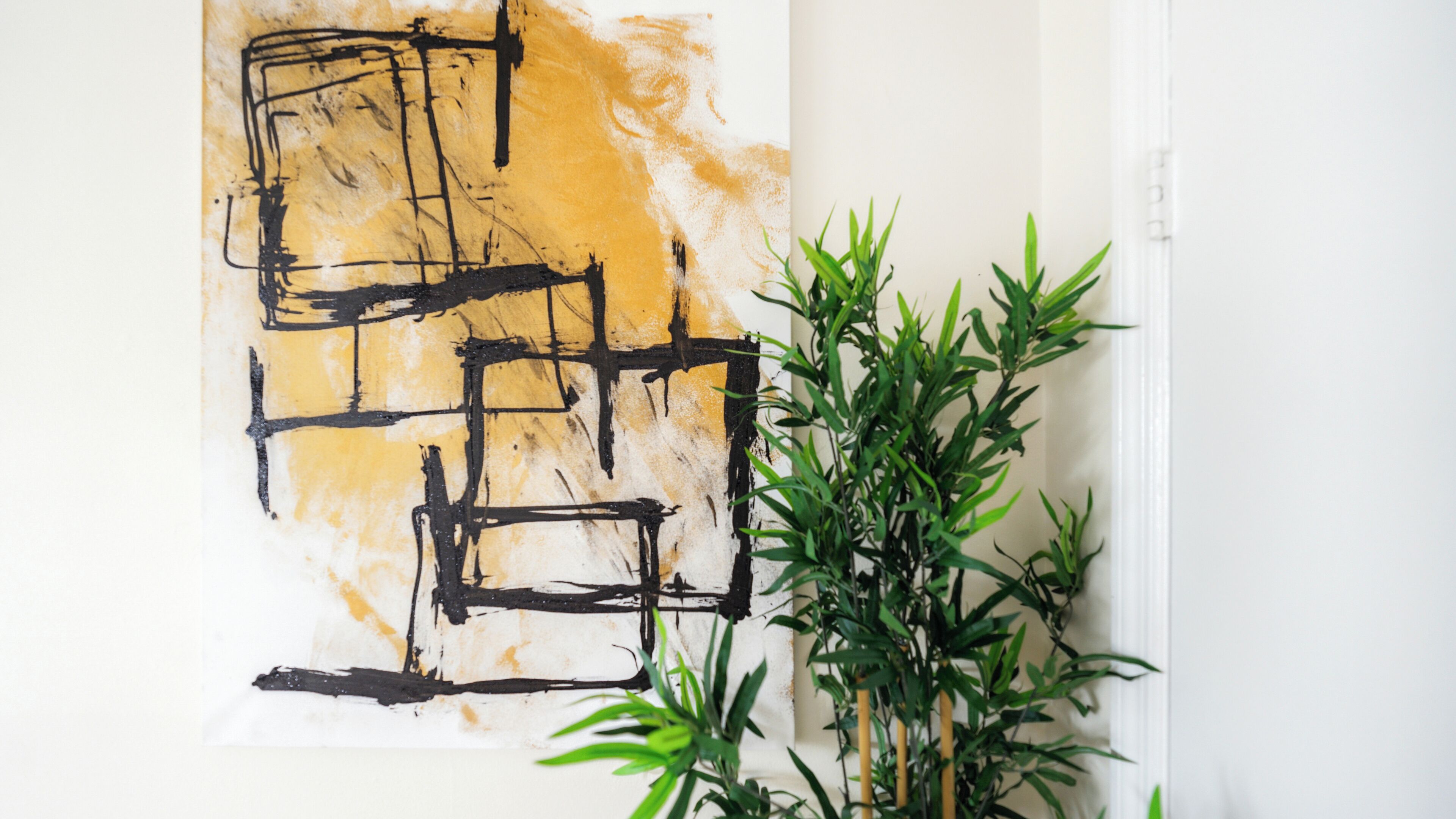 A wall with an abstract painting and a potted plant.