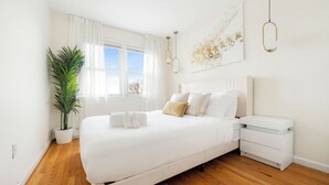 A modern bedroom with a large bed, bedside tables, a potted plant, and a view of the outdoors.