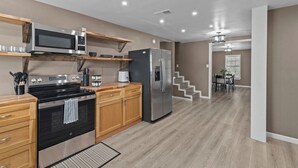 A modern kitchen with wooden cabinets, a stainless steel oven, a microwave, and a refrigerator. There is a wooden shelf above the microwave and a small table with a toaster. - 3-bedroom Rustic Retreat in Coushatta (Coushatta)
