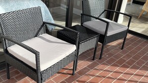 Een balkon met twee rieten stoelen en een glazen deur.