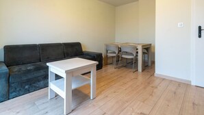 Ein Wohnzimmer mit einem dunkelgrauen Sofa, einem Holztisch und einem kleinen Esstisch mit vier Stühlen.