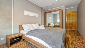 Ein modernes Schlafzimmer mit einem Holzbett, einem fest eingebauten Fernseher, einem großen Spiegel und einer Holztür.
