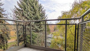 Ein Balkon mit Metallgeländer, Fliesenboden und Blick auf Bäume und Gebäude.