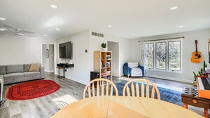 Un salon moderne avec un canapé gris, un tapis rouge, une table à manger en bois et une guitare.