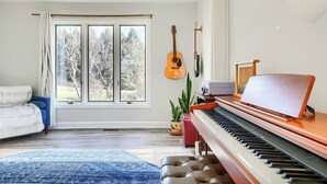 Une pièce avec un piano, une guitare, un canapé et une grande fenêtre avec des rideaux.