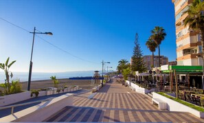 Eine Uferpromenade mit Strand, Palmen und einer Reihe von Restaurants.