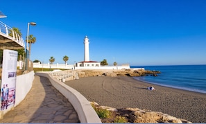 A coastal walkway leading to a lighthouse, with a clear sky and calm sea. - Wake up to the waves in this beachfront Torrox apartment. (Torrox Costa)