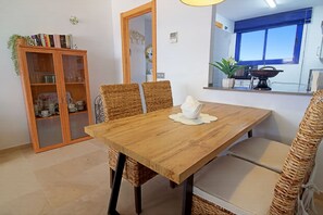 Ein Essbereich mit einem Holztisch, Korbstühlen und einem Schrank mit Glastüren.