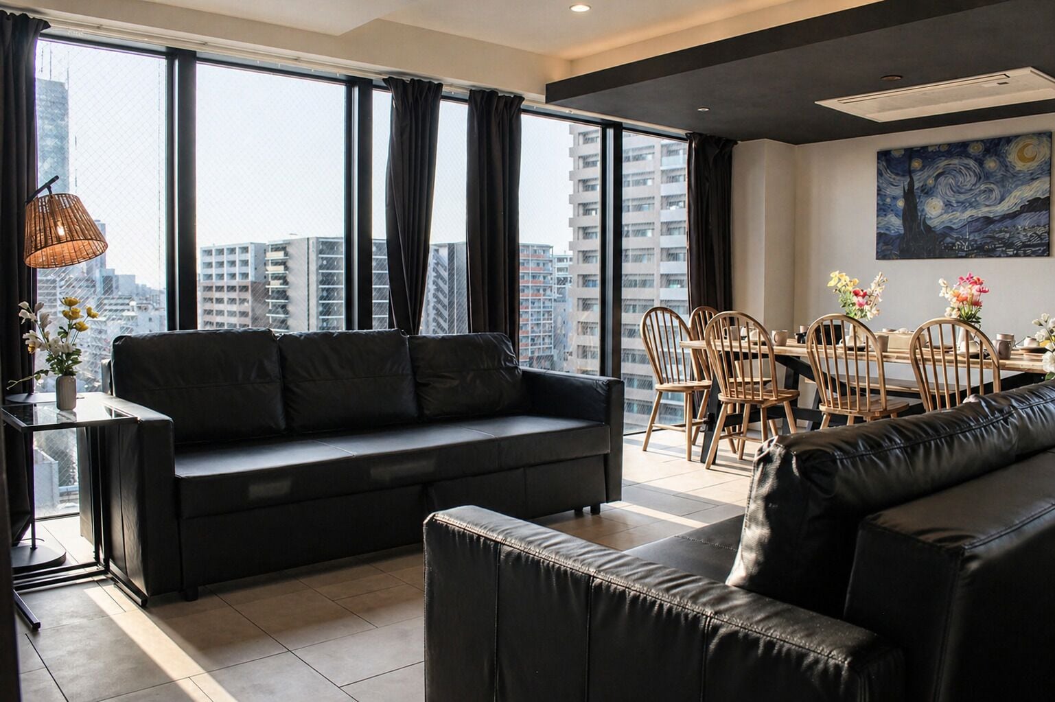 Una sala de estar moderna con un sofá de cuero negro, una mesa de comedor con sillas y un ventanal con cortinas.