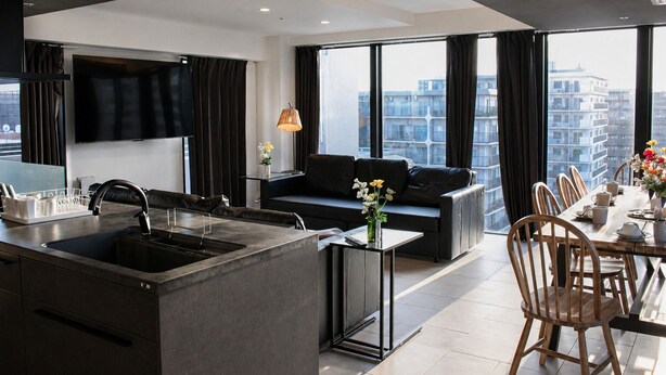 A modern kitchen with a central island, a dining area with a table set for six, and a living area with a sofa and a TV. - Osaka Namba River Side Garden Hotel (Osaka)