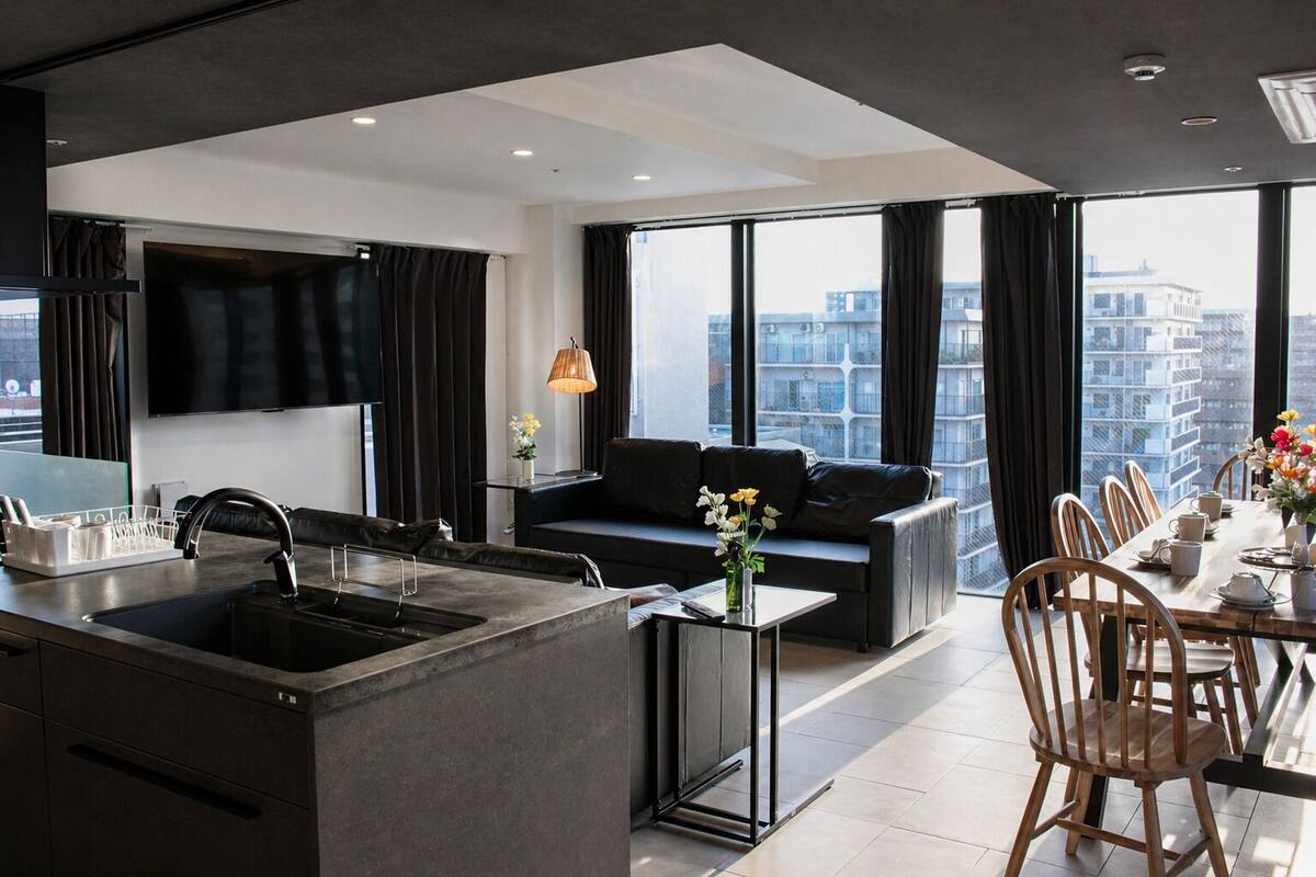 A modern kitchen with a central island, a dining area with a table set for six, and a living area with a sofa and a TV.