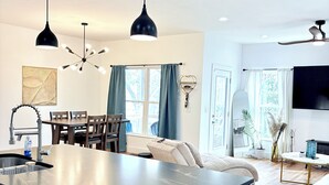 A modern kitchen with a central island, dining area with chairs, a sofa, and a TV in the living room.