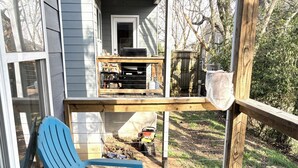 A wooden deck with blue chairs, a table, and a grill area.
