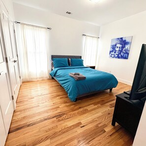 Ein Schlafzimmer mit einem Bett, Holzboden, einem Fernsehschrank und einem Gemälde an der Wand.