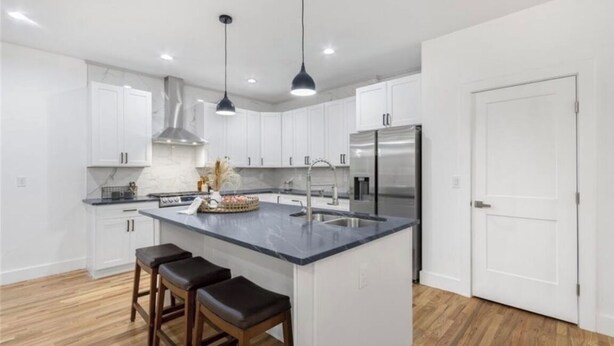 A modern kitchen with white cabinets, a central island with bar stools, stainless steel appliances, and pendant lighting.